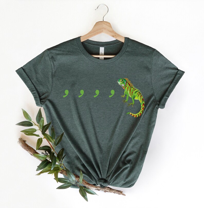 May include: A dark green t-shirt with a green and red iguana and four green commas printed on the front.
