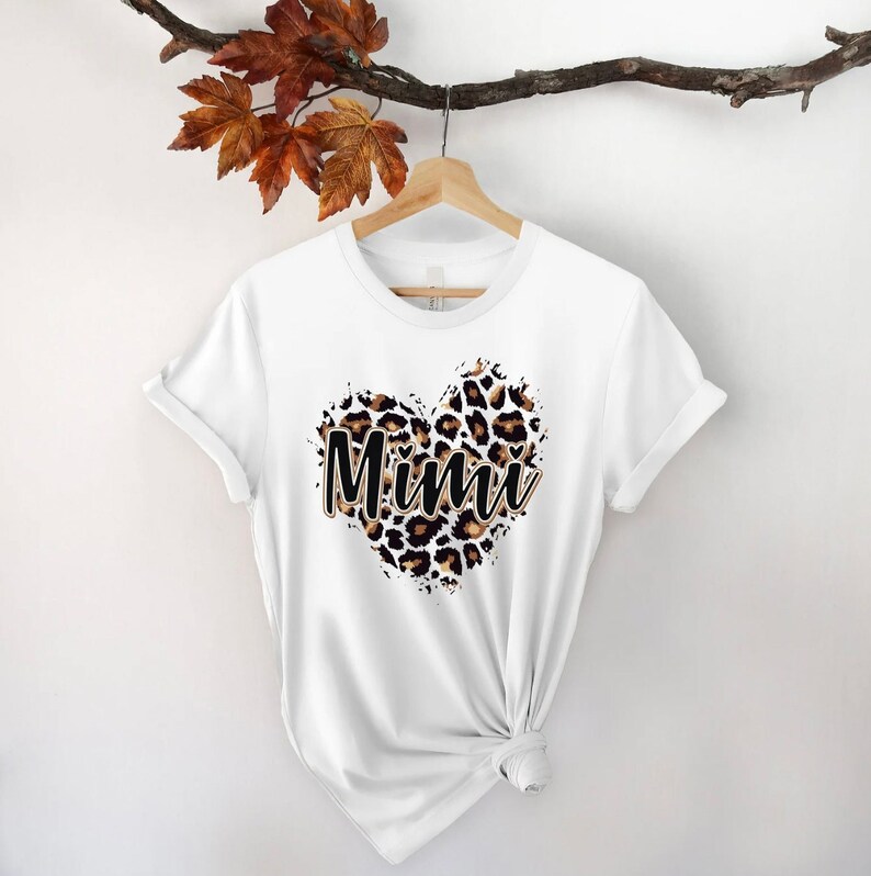May include: White t-shirt with a leopard print heart design and the word "Mimi" in black text.