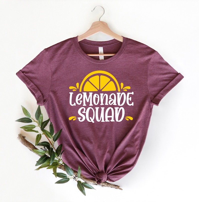 May include: A maroon t-shirt with a yellow lemon graphic and the text "Lemonade Squad" in white.