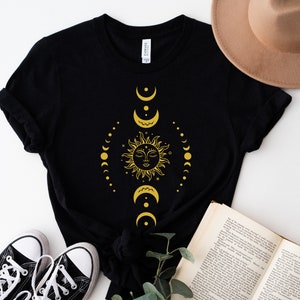 May include: Black t-shirt featuring a gold sun and moon design. The sun has a face and is surrounded by crescent moons and stars.