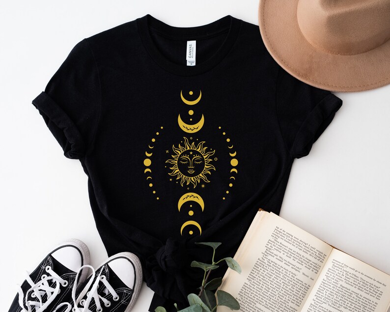 May include: Black t-shirt featuring a gold sun and moon design. The sun has a face and is surrounded by crescent moons and stars.