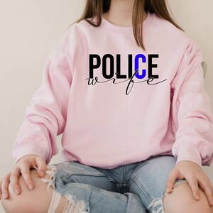 May include: Pink sweatshirt with the text "POLICE wife" in black lettering with a blue "C".
