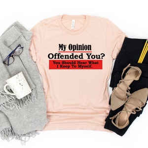 May include: A peach colored t-shirt with the text "My Opinion Offended You? You Should Hear What I Keep To Myself." in black and red lettering.