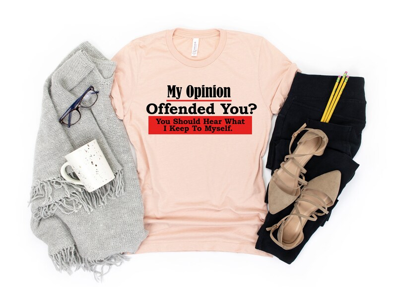 May include: A peach colored t-shirt with the text "My Opinion Offended You? You Should Hear What I Keep To Myself." in black and red lettering.