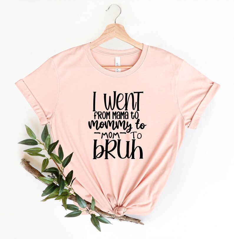 May include: A light pink t-shirt with a black graphic that reads "I went from mama to mommy to -mom- to bruh".