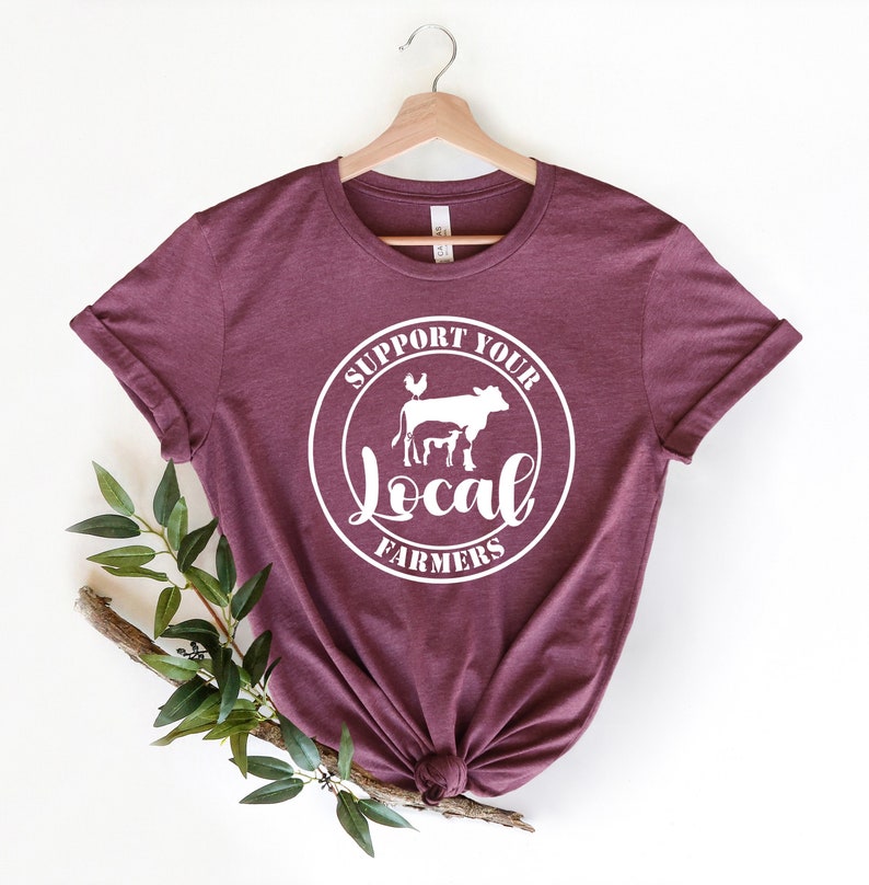 May include: A maroon t-shirt with a white circle graphic that says "Support Your Local Farmers" with a cow, calf, pig, and chicken inside the circle.