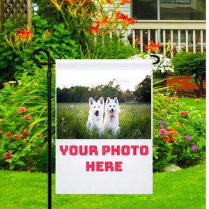 May include: A white garden flag with a photo of two white dogs sitting in a field. The text "YOUR PHOTO HERE" is printed in red on the flag.