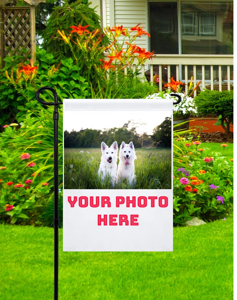 May include: A white garden flag with a photo of two white dogs sitting in a field. The text "YOUR PHOTO HERE" is printed in red on the flag.
