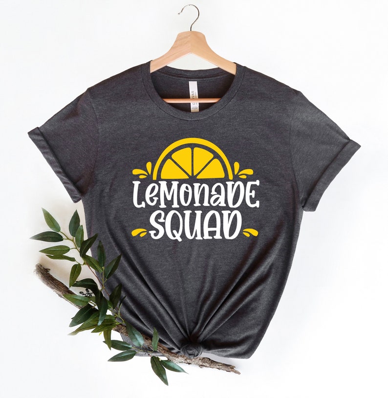 May include: A dark gray t-shirt with a white graphic that says "Lemonade Squad" and a yellow lemon slice graphic.