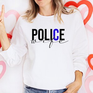 May include: A white sweatshirt with the text "POLICE wife" in black and blue lettering. The "C" in "POLICE" is blue.