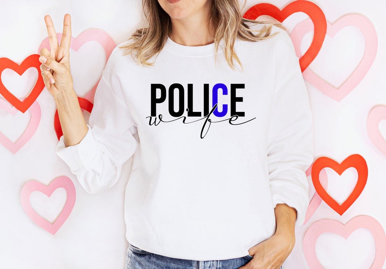 May include: A white sweatshirt with the text "POLICE wife" in black and blue lettering. The "C" in "POLICE" is blue.