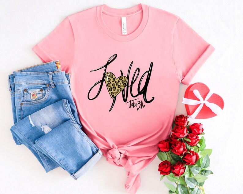 May include: Pink t-shirt with a black and gold leopard print heart and the word "Loved" written in black script. The text "John 3:16" is written in black script below the heart.