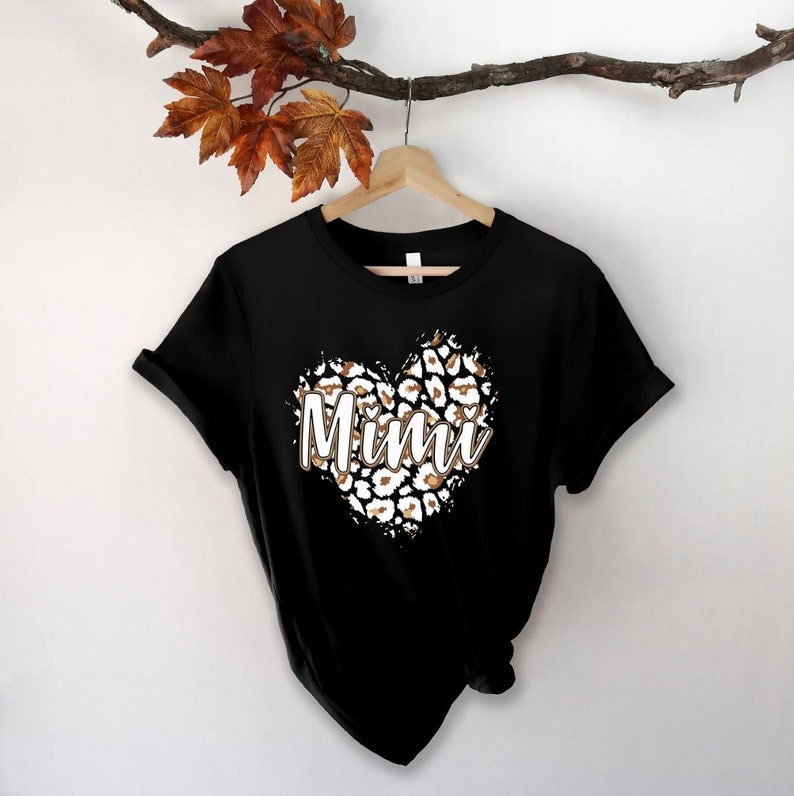 May include: Black t-shirt with a leopard print heart design and the word "Mimi" in white text.