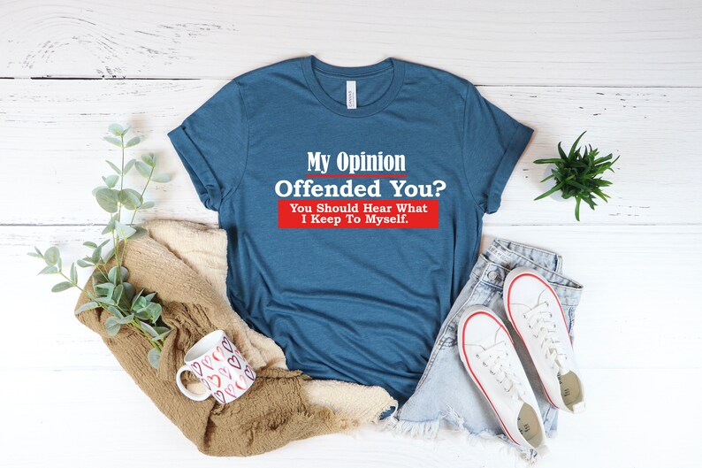 May include: A blue t-shirt with the text "My Opinion Offended You? You Should Hear What I Keep To Myself." printed in white on a red background.