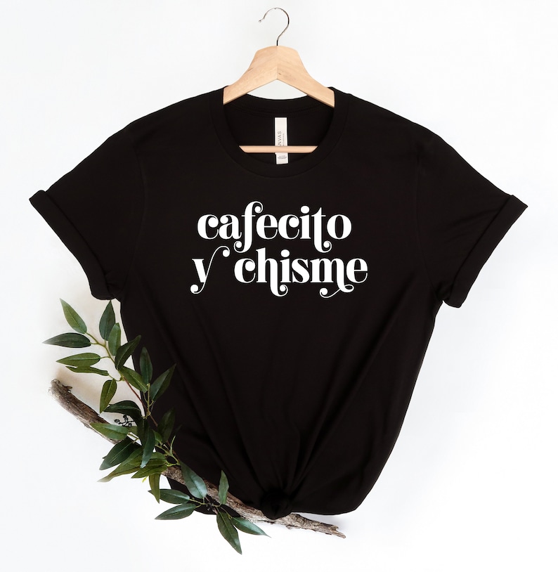 May include: Black t-shirt with white text that reads "cafecito y chisme" in a retro font.