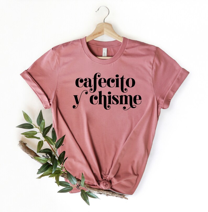 May include: A mauve t-shirt with the text "cafecito y chisme" in black retro-style lettering.