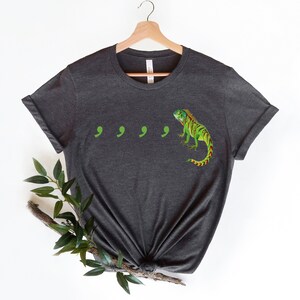 May include: Dark gray t-shirt with a green iguana and four green commas printed on the front.