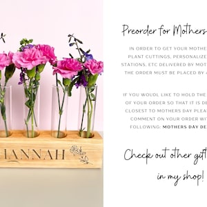 Pu&ograve; includere: Un vaso di legno con il nome "HANNAH" inciso su di esso. Il vaso contiene cinque provette di vetro, ciascuna contenente un fiore rosa. Il testo "Preorder for Mothers Day!!!" &egrave; visibile sullo sfondo.