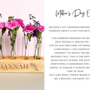 May include: A wooden flower vase with five glass tubes, holding pink and purple flowers. The vase is engraved with the name "HANNAH" and floral designs. Text above reads "Mother's Day Orders".