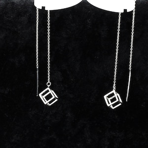 May include: A pair of silver threader earrings. Each earring has a fine chain with a small, open cube pendant and a straight bar. The earrings are displayed against a black backdrop.