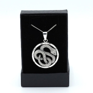 May include: A silver necklace with a round pendant featuring a snake design. The pendant is in a black velvet box.