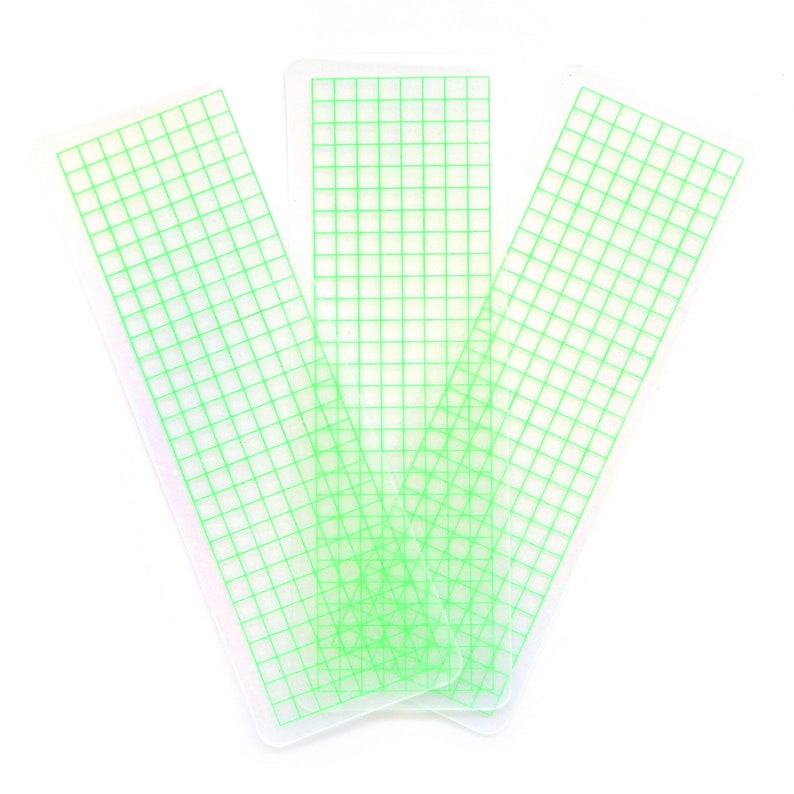 May include: Three clear plastic rulers with a green grid pattern. The rulers are stacked on top of each other.