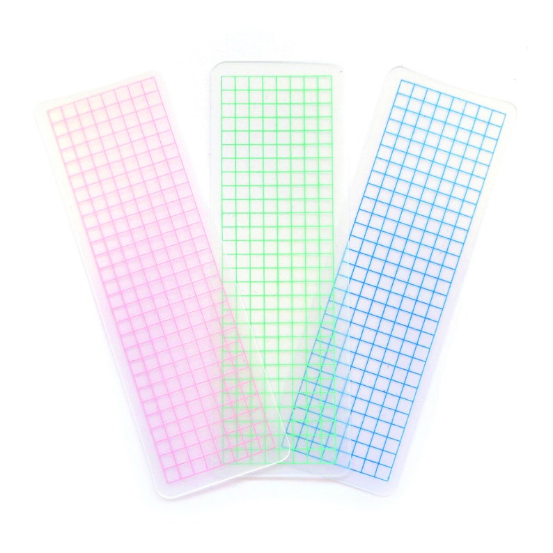 May include: Three clear plastic grid rulers with pink, green, and blue grid lines.