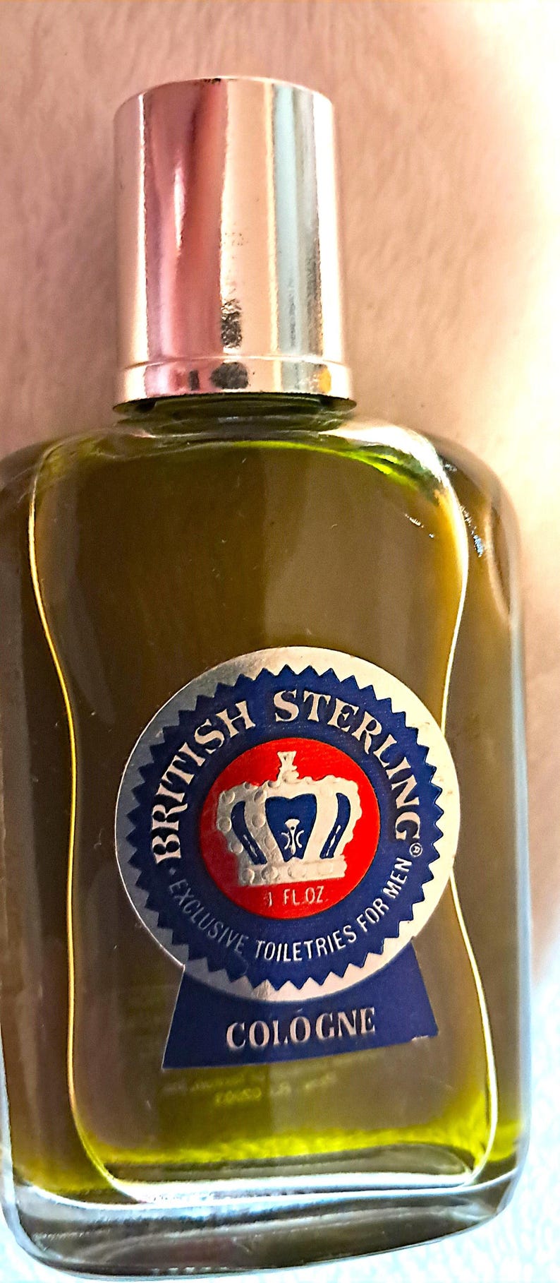 May include: A vintage cologne bottle with a silver cap and a green liquid. The label reads "British Sterling" with a crown emblem and "Exclusive Toiletries For Men". The bottle contains 1 fl oz of cologne.