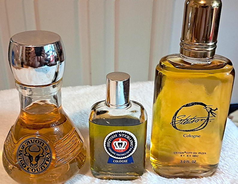 May include: Three vintage cologne bottles. The bottle on the left has a silver cap and a Wild Country logo. The middle bottle is labeled British Sterling Cologne. The bottle on the right is labeled Stetson Cologne, 3.0 fl oz.