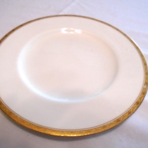 May include: A white ceramic plate with a gold rim. The plate is round and has a smooth surface.