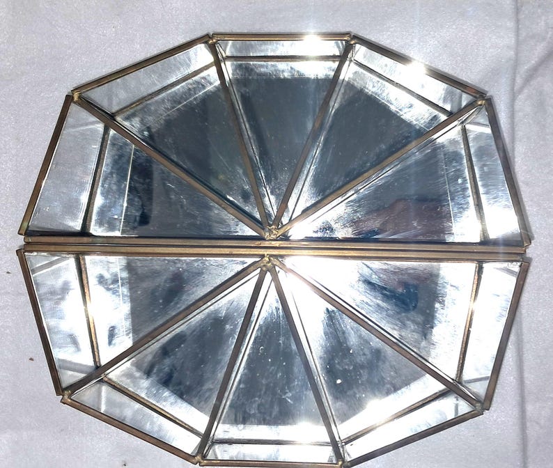 Op de afbeelding: Een geometrische decoratieve doos van glas en metaal met een scharnierend deksel. De doos bestaat uit meerdere driehoekige en trapeziumvormige glazen panelen, omlijst door dun, goudkleurig metaal. De doos is open en onthult het interieur.