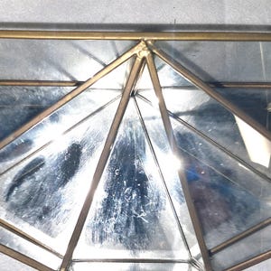 Op de afbeelding: Geometrisch glazen terrarium met een messingkleurig metalen frame. Het terrarium heeft meerdere driehoekige en trapeziumvormige glazen panelen, waardoor een veelzijdige vorm ontstaat. Het messing frame voegt een vleugje elegantie toe. Ideaal voor planten.