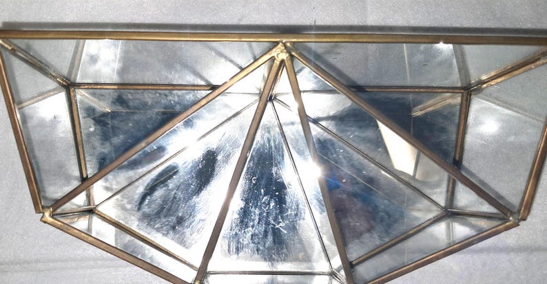 Op de afbeelding: Geometrisch glazen terrarium met een messingkleurig metalen frame. Het terrarium heeft meerdere driehoekige en trapeziumvormige glazen panelen, waardoor een veelzijdige vorm ontstaat. Het messing frame voegt een vleugje elegantie toe. Ideaal voor planten.