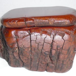 May include: A handcrafted wooden box with a lid. The box is a rich, dark brown color with a glossy finish on the lid. The body of the box has a textured, cracked appearance, giving it a rustic, aged look. The box is likely used for storage or display.