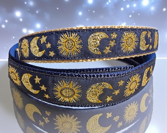 May include: A dark navy blue ribbon featuring a repeating embroidered pattern of golden suns, crescent moons, and small stars. The ribbon has a smooth texture with metallic gold thread detailing and a finished edge, coiled in a circular shape.