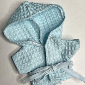 K&ouml;nnte beinhalten: Ein hellblauer Kapuzenbademantel mit gestepptem Muster und einem passenden Bindeg&uuml;rtel.