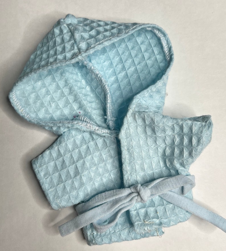 K&ouml;nnte beinhalten: Ein hellblauer Kapuzenbademantel mit gestepptem Muster und einem passenden Bindeg&uuml;rtel.