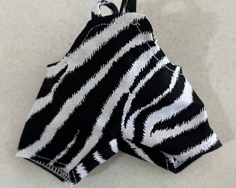 Könnte beinhalten: Eine kurze Hose mit schwarz-weißem Zebramuster. Das Kleidungsstück hat ein hoch tailliertes Design mit einer kleinen Stoffschlaufe in der Mitte des Bundes und genähten Beinöffnungen, gefertigt aus einem gewebten Textilmaterial.