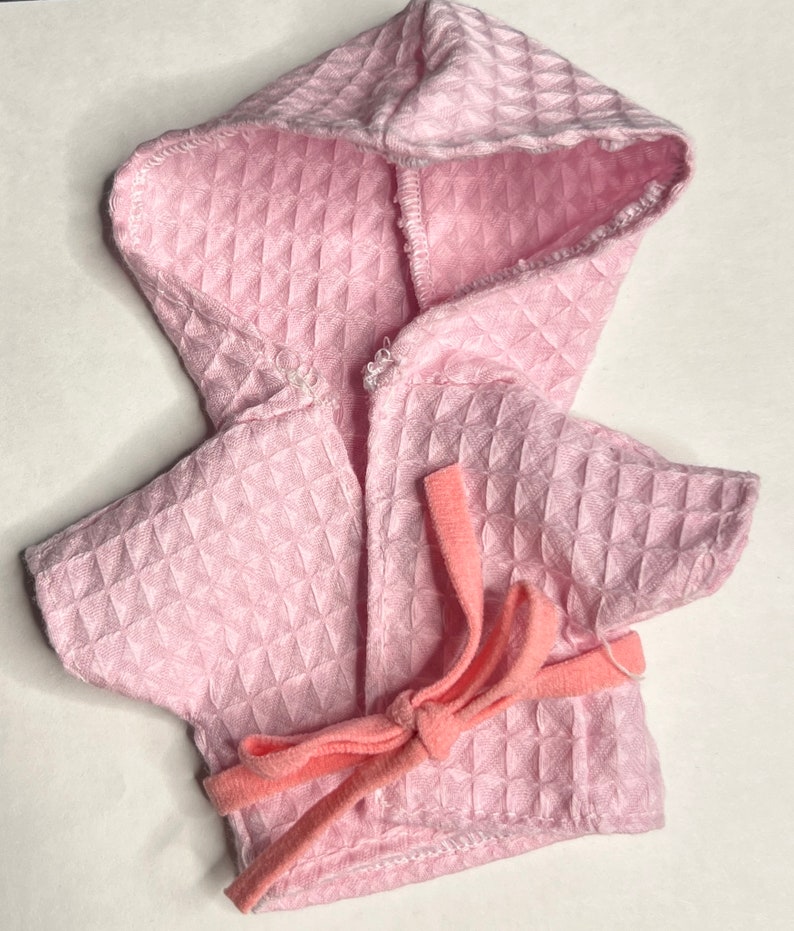 K&ouml;nnte beinhalten: Ein rosa Waffel-Struktur-Bademantel mit Kapuze und einem rosa Bindeg&uuml;rtel.