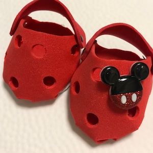 May include: A pair of red foam Mickey Mouse character clogs with black ears and a red and white polka dot button.
