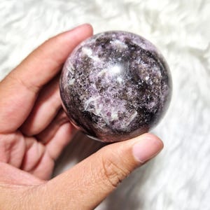 Peut inclure: Une sphère de cristal violette et noire avec un motif tourbillonnant. La sphère est lisse et polie.