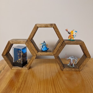 May include: A wooden hexagonal shelf unit with three shelves. The shelves are decorated with miniature figurines and a dice tower. The figurines are painted in blue, orange, and silver.