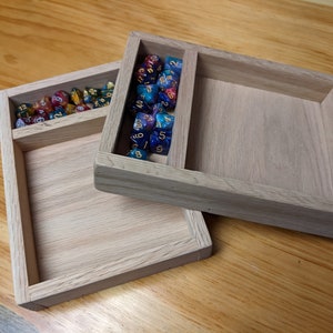 Puede incluir: Dos bandejas de madera con un compartimento para dados. La bandeja superior tiene una variedad de dados coloridos con n&uacute;meros dorados. La bandeja inferior est&aacute; vac&iacute;a.