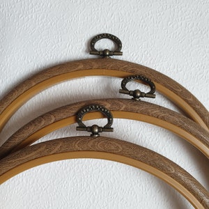 May include: Three brown wooden embroidery hoops with brass rings. The hoops are nested inside each other, with the largest hoop at the bottom and the smallest hoop at the top.
