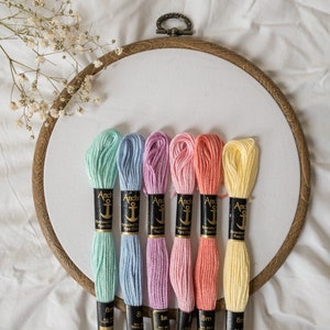 May include: Six spools of Anchor Stranded Cotton embroidery floss in pastel colours: light green, light blue, lavender, pink, coral, and yellow. Each spool has a black label with the Anchor logo and the text "Stranded Cotton Fast Color" and "8m Art. 4312 100% Cotton".