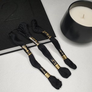 May include: Three spools of black embroidery floss with gold labels that read "Anchor Embroidery Floss 8m Black".