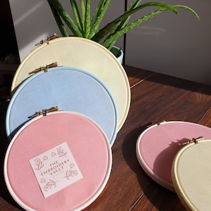 May include: Four embroidery hoops in different sizes, with a pale yellow, light blue, pink, and a pale yellow hoop. The pink hoop has a sticker that says "The Embroidery Vault".