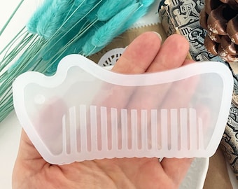 May include: A clear, comb-shaped mold with a wavy edge and vertical teeth. The mold is held in a hand, with a background of turquoise dried flowers and a decorative item. This item is likely used for crafting or creating resin combs.