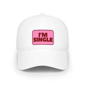 May include: A white baseball cap featuring a rectangular pink patch on the front panel. The patch has a dark brown border and displays the text I'M SINGLE in bold, dark brown, capital letters centered within the pink rectangular background.