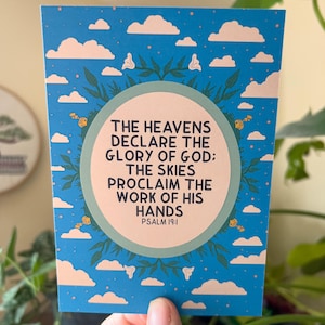 Può includere: Un biglietto blu e bianco con una citazione dal Salmo 19:1. La citazione recita: "I cieli narrano la gloria di Dio: I cieli proclamano l'opera delle sue mani".